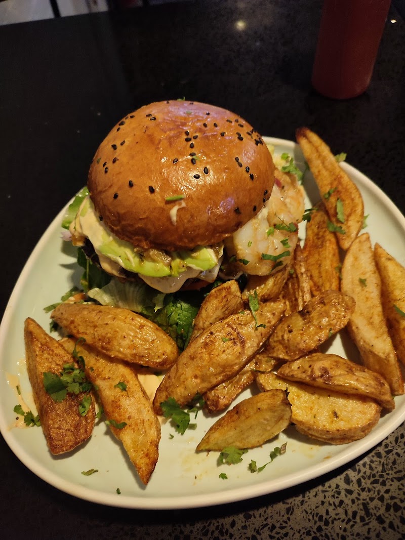 Hamburguesa Res & Pez con aguacate y camarones sobre la carne, acompañada de papas en gajos